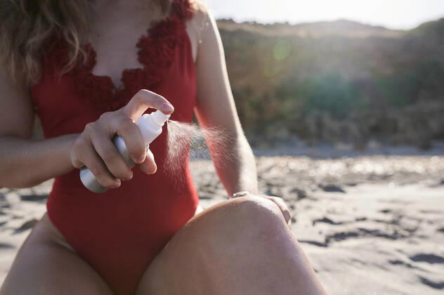 Young woman applying suncream spray on the beach model released Symbolfoto  IGGF01319