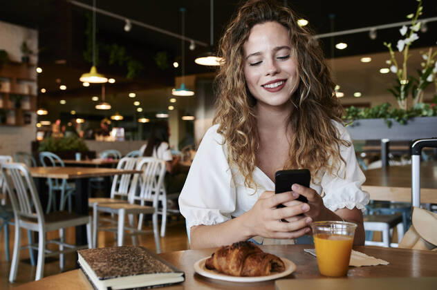 Smiling young woman using smartphone in a cafe while having breakfast model released Symbolfoto  IGGF01332