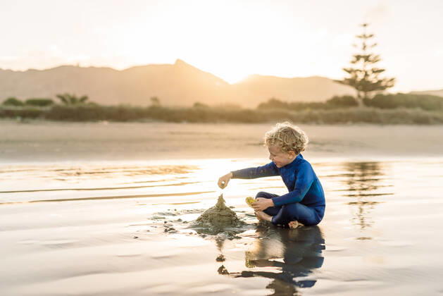 Young child building sandcastle at beach in New Zealand at dusk New Zealand, Hawke s Bay, Waimarama R_JUCR191021-226980-01