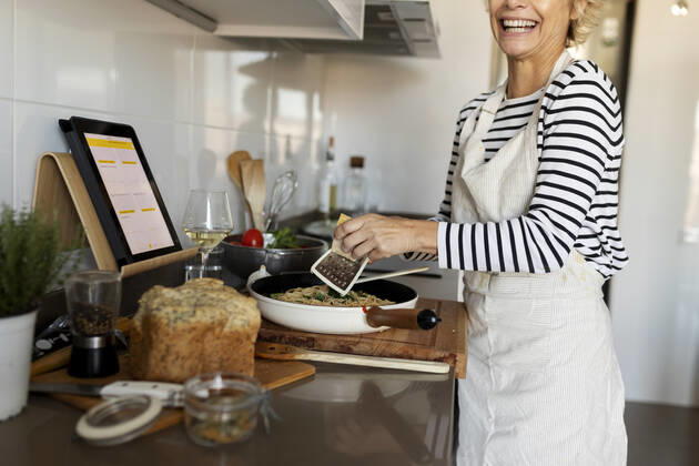 Happy mature woman with tablet cooking pasta dish in kitchen at home model released Symbolfoto property released  VABF02448
