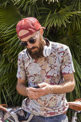 Mature man with red basecap, sunglasses and white headphones using smartphone model released Symbolfoto TCF06223