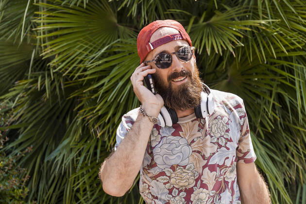 Mature man with red basecap, sunglasses and white headphones using smartphone model released Symbolfoto TCF06225