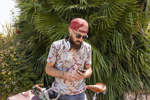 Mature man with red basecap, sunglasses and white headphones using smartphone model released Symbolfoto TCF06226