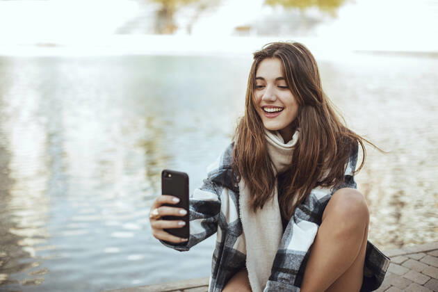 Young brunette woman using smartphone and taking a selfie at lake model released Symbolfoto  ACPF00659