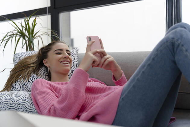 Portrait of happy young woman lying on the couch using cell phone model released Symbolfoto property released  ERRF02579