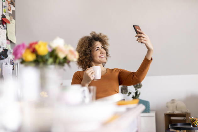 Woman holding coffee cup and taking a selfie at home model released Symbolfoto property released  FMKF06072