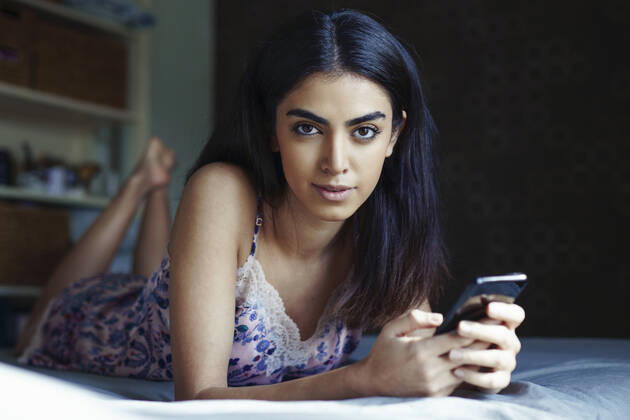Portrait of young woman lying on bed with smartphone model released Symbolfoto  JSMF01429