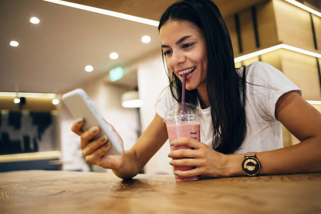 Black-haired woman drinking a smoothie and using smartphone in cafe model released Symbolfoto  OYF00102