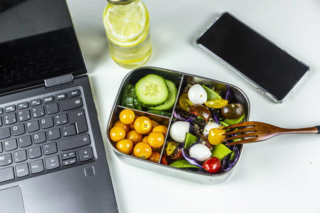 Laptop, smart phone, bottle of lemonade and lunchbox with cucumber slices, winter cherries and quinoa salad (quinoa, cherry tomato, red cabbage, sugar snap peas and mozzarella balls)  SARF04410