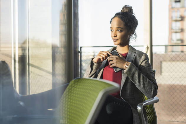 Young businesswoman with cell phone sitting at the window in office model released Symbolfoto property released  UUF20029