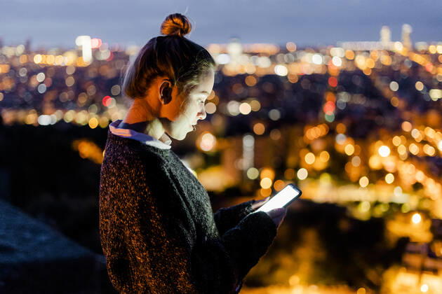 Young woman sitting on railing above the city using cell phone, Barcelona, Spain model released Symbolfoto GIOF07939