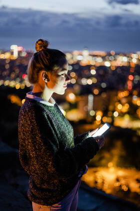 Young woman sitting on railing above the city using cell phone, Barcelona, Spain model released Symbolfoto GIOF07940