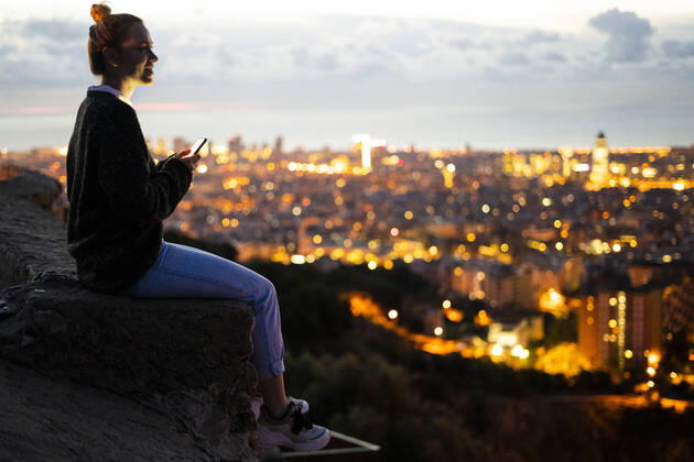 Young woman sitting on railing above the city using cell phone, Barcelona, Spain model released Symbolfoto GIOF07941