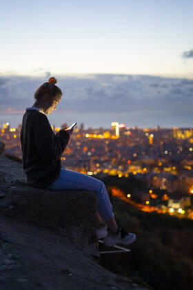 Young woman sitting on railing above the city using cell phone, Barcelona, Spain model released Symbolfoto GIOF07942