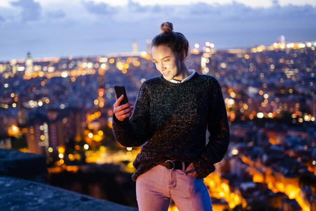 Young woman sitting on railing above the city using cell phone, Barcelona, Spain model released Symbolfoto GIOF07943