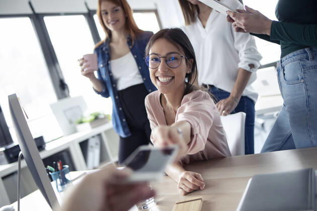 Smiling businesswoman giving a smartphone to her colleague model released Symbolfoto property released  JSRF00850
