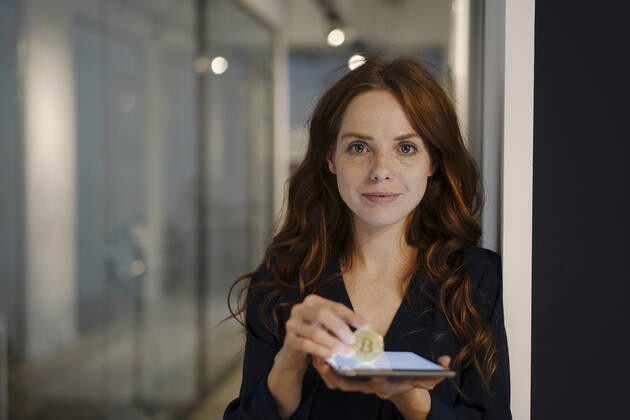 IMAGO Creative: 2022 Aussichten IMAGO Creative: 2021 Trends Portrait of redheaded woman holding bitcoin and tablet on office floor model released Symbolfoto property released  KNSF07182
