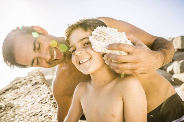 Father and son having fun on the beach and listening to the ocean in a shell model released Symbolfoto  SDAHF00486