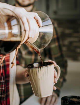 hot coffee is poured from a pour over into a tan coffee cup Poland, ME, United States ,model released, Symbolfoto CR_SSNF200327-319274-01