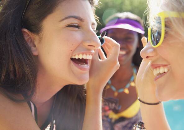 Happy teenage girl friends applying mascara on sunny patio England Kent  Copyright: JuttaxKlee fStopImages1889048