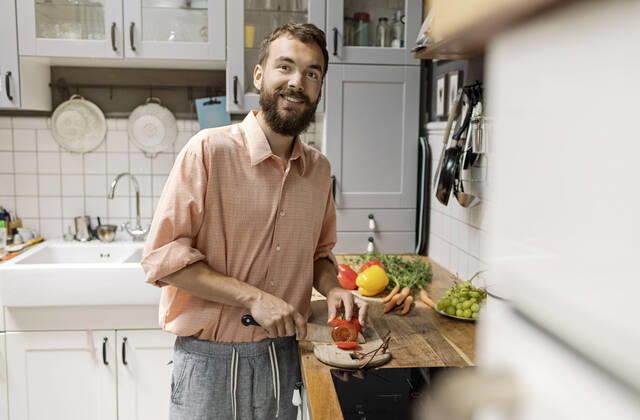 Young man standing in kitchen, chopping tomatoes, smiling model released Symbolfoto property released  PESF01808