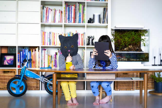 Two girls sitting at table, hiding behind digital tablet and cat mask model released Symbolfoto property released ERRF03440