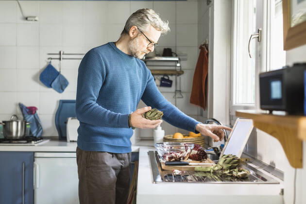 Mature man preparing salad in his kitchen using digital tablet model released Symbolfoto property released MCVF00259