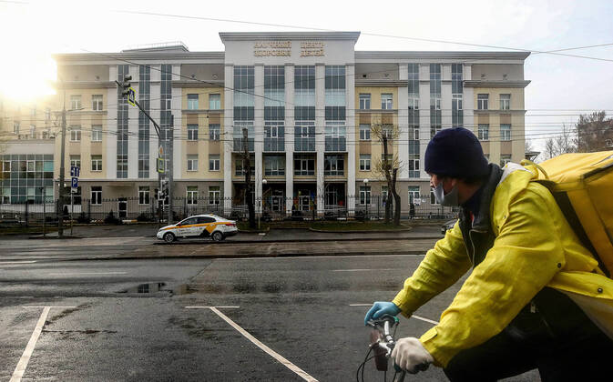 MOSCOW, RUSSIA - APRIL 24, 2020: A food delivery worker rides a bicycle past the building of the National Medical Research Centre for Children s Health (NMITS) during the pandemic of the novel coronavirus disease (COVID-19). Part of the research centre has been converted to treat young patients with suspected or confirmed novel coronavirus infection (COVID-19). Valery Sharifulin TASS  TS0D7031