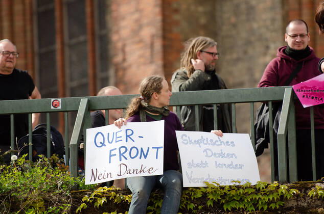 Lockdown immediately end demonstration on Südermarkt in Flensburg The Communication Centre for Democratic Resistance is organising a demonstration on 25 04 2020 in Flensburg on Südermarkt, city centre here counter-demonstrator, Hanna Poddig is sitting on the Südermarkt platform, holding up banners with the words Querfront nein Dank and Skpetisches Denken statt kruder Verschwörung