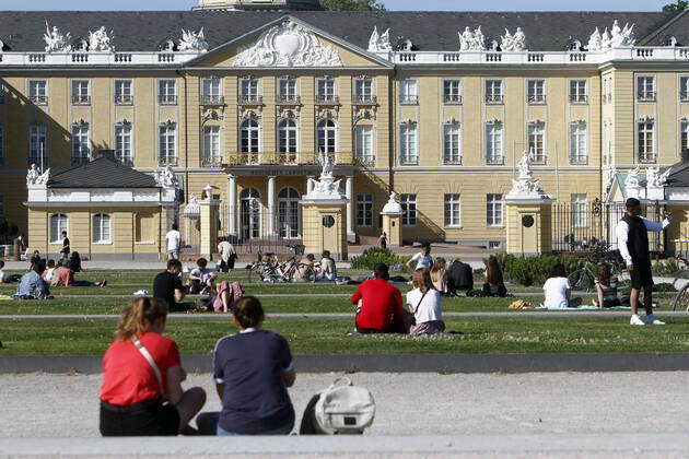 People sit on the lawns on the Schlossplatz in front of the Landesmuseum and the palace, respecting the rules of distance, and enjoy the warm spring day in the city centre of Karlsruhe, r City centre of Karlsruhe, Baden Württemberg, Germany