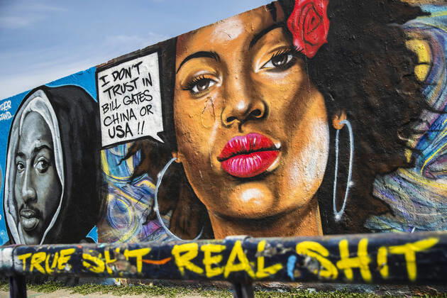 Graffiti of the artist Eme Freethinker with a woman with a speech bubble I dont trust Bill Gates, CHina or USa kissing with a face mask, at Mauerpark in Berlin on April 28, 2020 Since yesterday it is mandatory to wear a protection for nose and mouth in trains, trams and busses Since tomorrow it is also mandatory for retail Coronavirus in Berlin