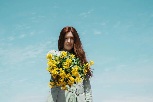 Portrait of redheaded young woman against sky presenting bunch of yellow flowers model released Symbolfoto AFVF06149