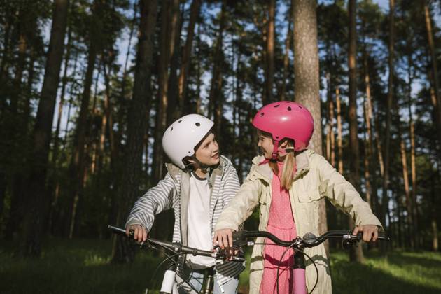 IMAGO Creative: Klimawandel - Umwelterziehung Girl and boy talking while riding bicycles in forest model released Symbolfoto EYAF01084