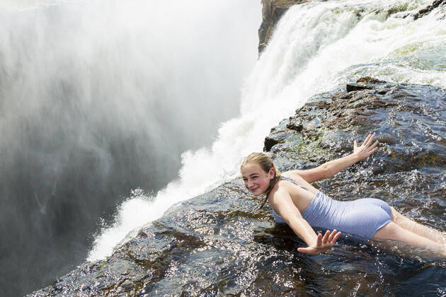 Young girl in the water at the Devils Pool lying on her front, arms spread out, at the edge of the cliff of Victoria Falls. Victoria Falls,Zambia,Young girl in the water at the Devils Pool lying on her front, arms spread out, at the edge of the cliff of Victoria Falls. Young girl in the water at the Devils Pool lying on her front, arms spread out, at the edge of the cliff of Victoria Falls.