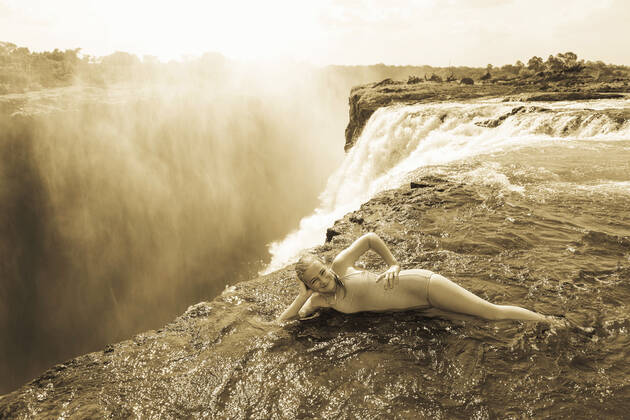 Young girl in the water at the Devils Pool leaning on her elbow, at the edge of the cliff of Victoria Falls. Victoria Falls,Zambia,Young girl in the water at the Devils Pool leaning on her elbow, at the edge of the cliff of Victoria Falls. Young girl in the water at the Devils Pool leaning on her elbow, at the edge of the cliff of Victoria Falls.