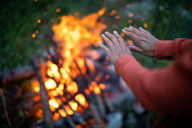  Young woman making fire while camping outdoors, in an alpine wilderness - warming up her hands near the fire Copyright: xLightpoetx Panthermedia27231751 ,model released, Symbolfoto