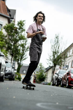 Smiling male barista holding coffee cup while skateboarding on road in city model released Symbolfoto KNSF08169