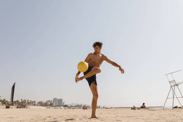 IMAGO Creative: Sommer Sport - Strand Shirtless male athlete playing with ball at beach against clear sky on sunny day model released Symbolfoto VABF03117