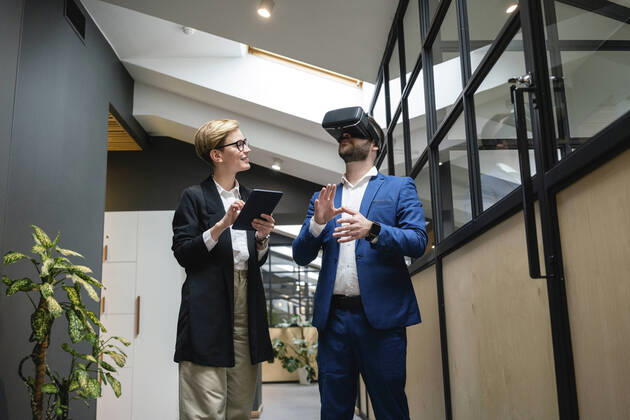 IMAGO Creative: 2022 Aussichten Businesswoman analyzing colleague using virtual simulation headset in creative office corridor model released Symbolfoto property released VPIF02662