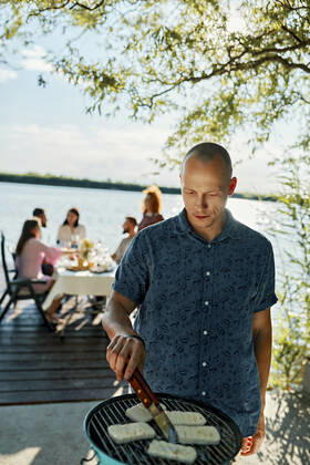 Man grilling Halloumi cheese at a lake with friends in background model released Symbolfoto ZEDF03564