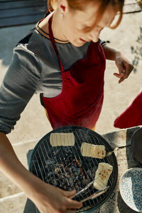 Woman preparing Halloumi cheese on barbecue grill ZEDF03565