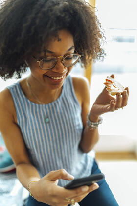 Close-up of smiling businesswoman with curly hair holding bread while using smart phone at home model released Symbolfoto property released BOYF01528