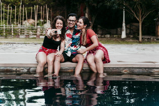 Smiling friends taking selfie while sitting at pool side model released Symbolfoto property released EBBF00732