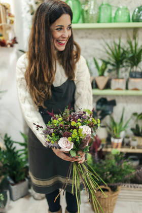 Smiling woman holding bunch of flowers while standing at flower shop model released Symbolfoto property released MRRF00400