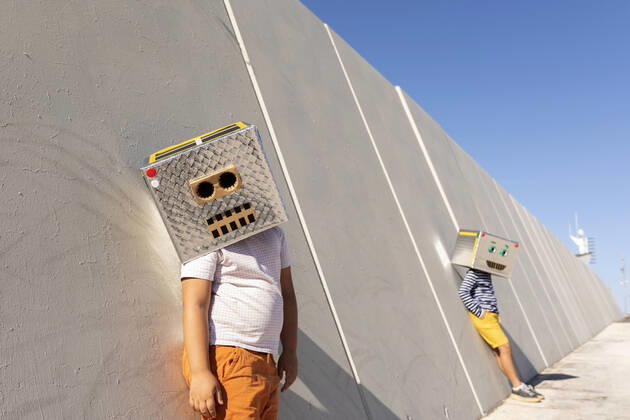 Boys wearing robot masks standing against wall in city on sunny day model released Symbolfoto VABF03132