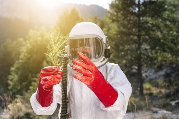 IMAGO Creative: Klimawandel - Zukunft und Innovation Close-up of male astronaut holding plant while standing against trees model released Symbolfoto JCMF01434