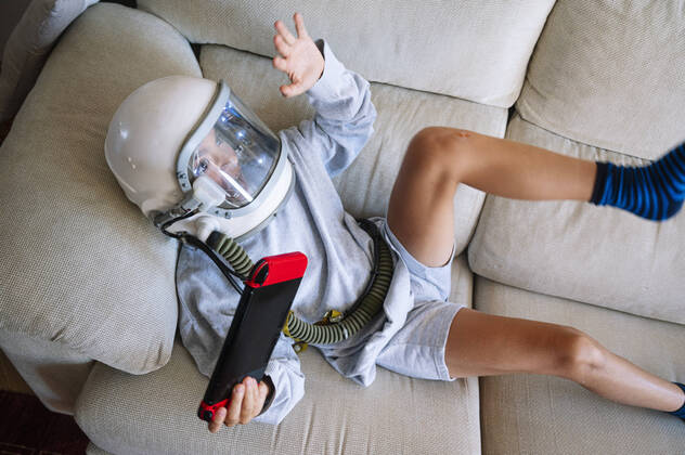 Boy wearing space helmet gesturing while playing video game sofa at home model released Symbolfoto property released JCMF01459