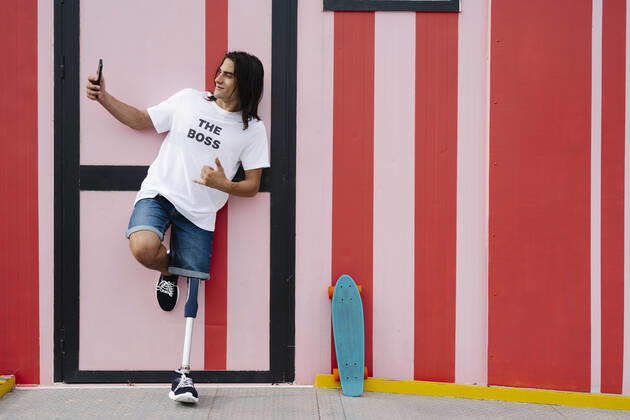 Disabled man taking selfie while standing against red wall model released Symbolfoto JCZF00315