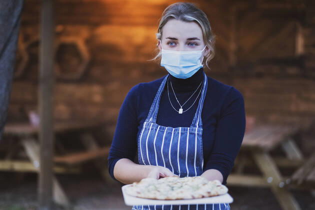 IMAGO Creative: Landleben - Essen Woman waitress in apron and face mask holding fresh pizza on a board Pizza Restaurant,United Kingdom,Woman waitress in apron and face mask holding fresh pizza on a board  Woman waitress in apron and face mask holding fresh pizza on a board