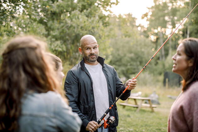 Father with fishing rod talking to daughters while standing by partner in yard, MA82747, Sweden, Stockholm Archipelago, model released Copyright: xMaskotx